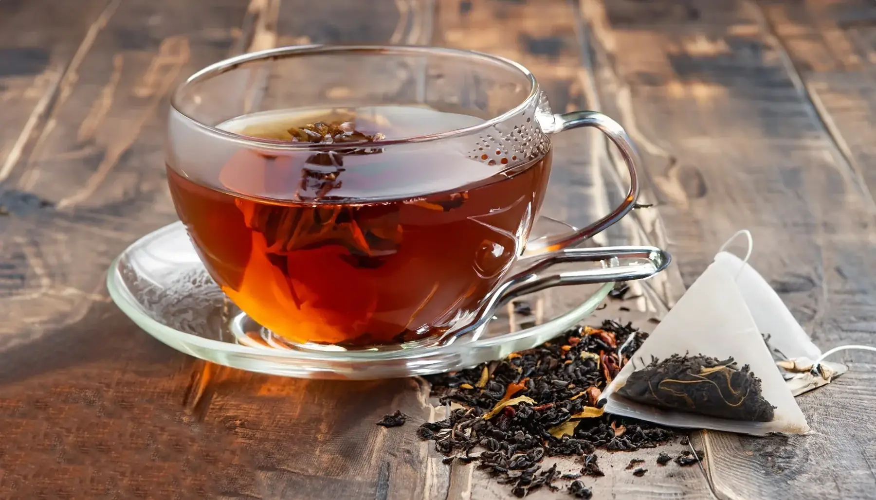 Glass cup of tea beside loose tea leaves and a pyramid tea bag