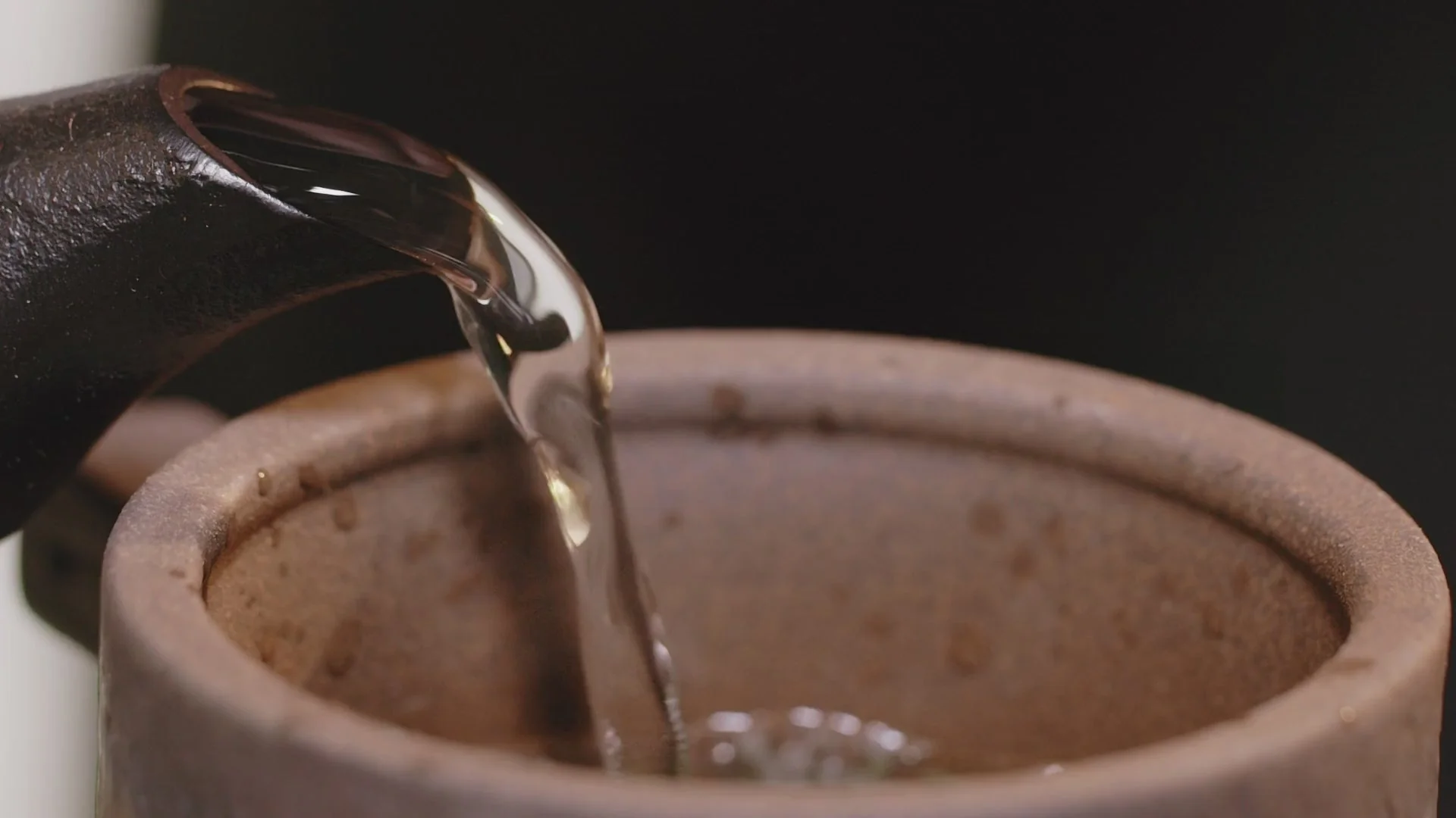 Tea being poured from a dark teapot into a ceramic cup, from the East to West store
