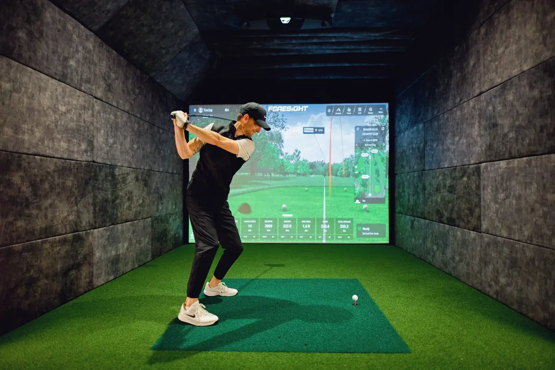 A golfer taking a swing in a Tee’d Up indoor golf simulator